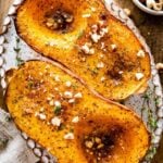 Baked butternut squash on a platter with nuts and herbs as seasoning.
