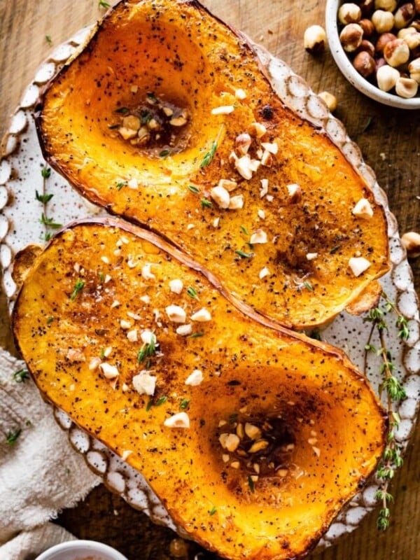 Baked butternut squash on a platter with nuts and herbs as seasoning.