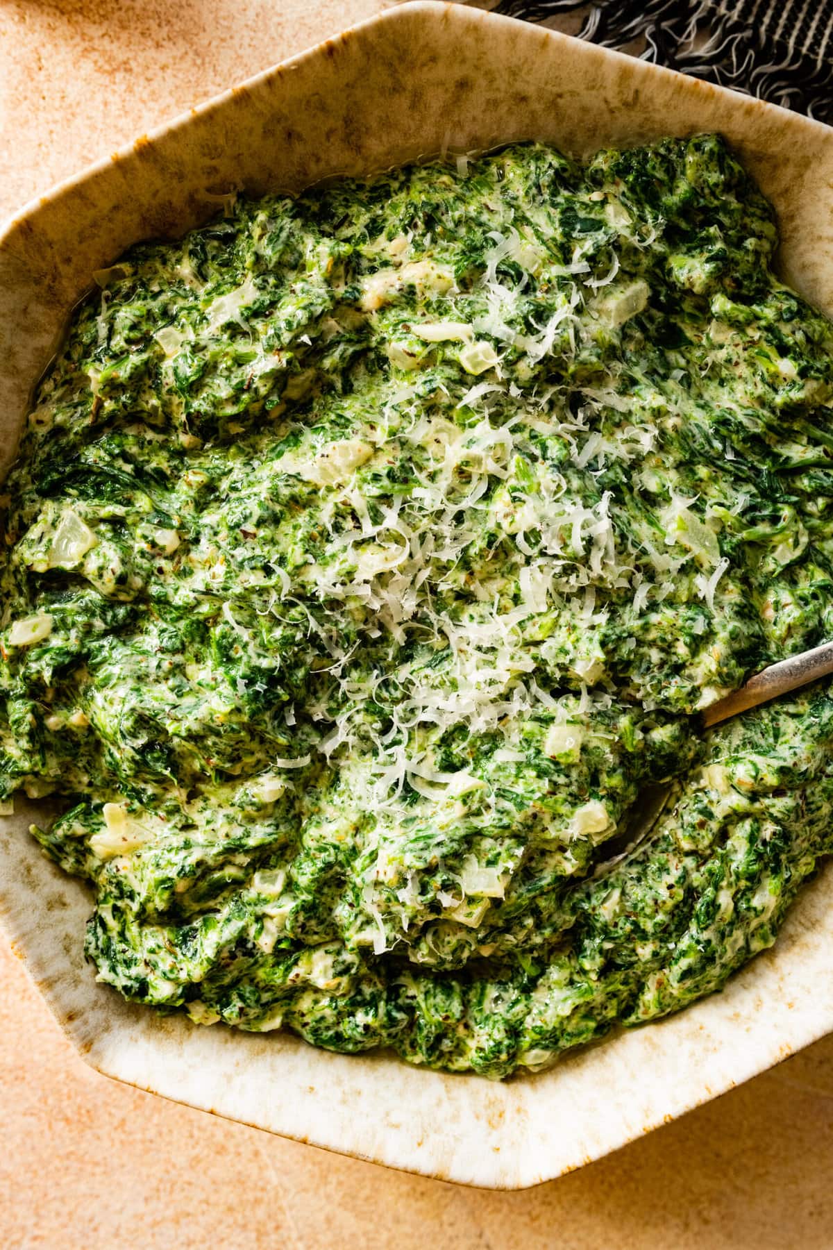 steakhouse creamed spinach recipe with a spoon in it. Cheese on top.