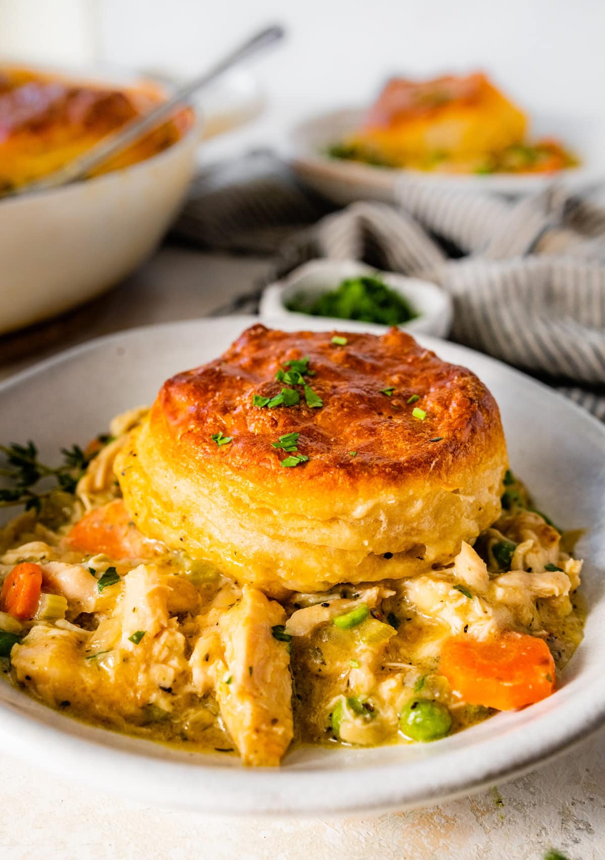 bowl of chicken pot pie casserole with biscuits in a bowl. One biscuit in the bowl with filling.