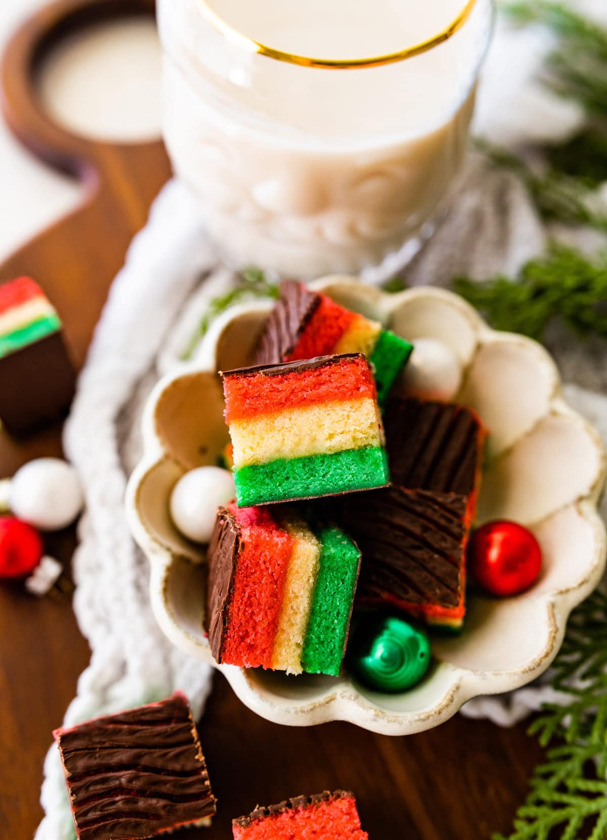 plate of Classic Italian Rainbow Cookies Recipe with cute Christmas ornaments around the platter. A glass of milk next to the cookie plate.