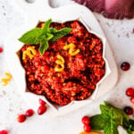 Fresh cranberry relish in a serving bowl with cranberries around it. Orange slices on the side.