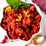 Fresh cranberry relish in a serving bowl with cranberries around it. Gold spoon next to it.