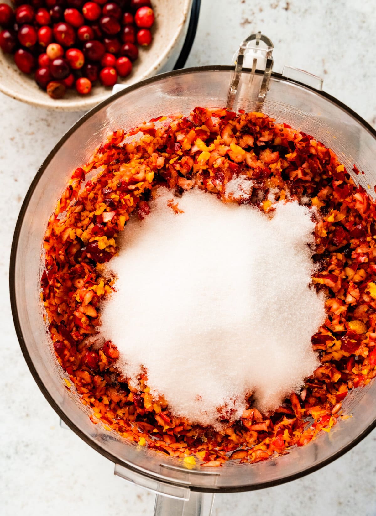 How to make easy fresh cranberry relish step-by-step: adding sugar to the oranges and cranberries in the food processor.