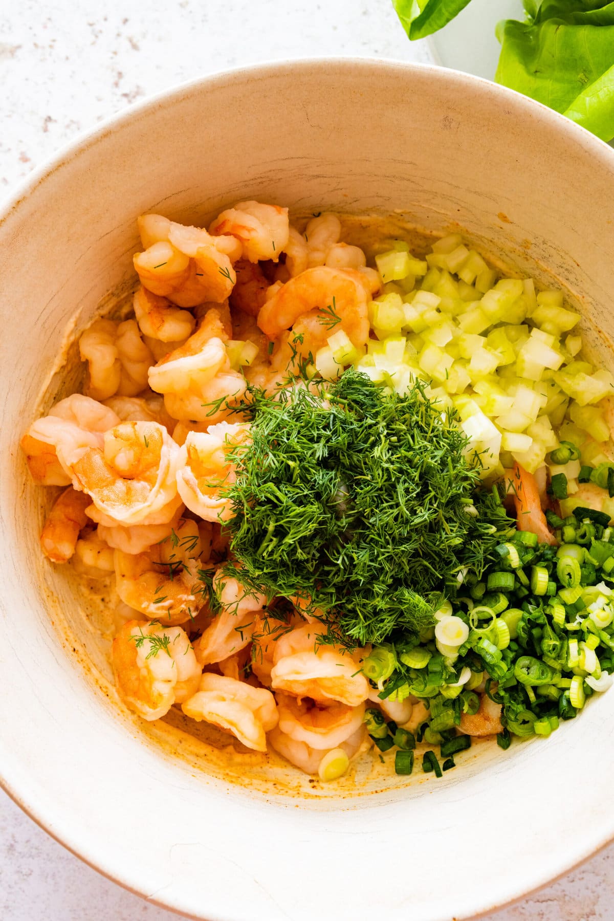 how to make shrimp salad step-by-step: adding all the ingredients in a bowl (herbs, shrimp, dressing, and celery).