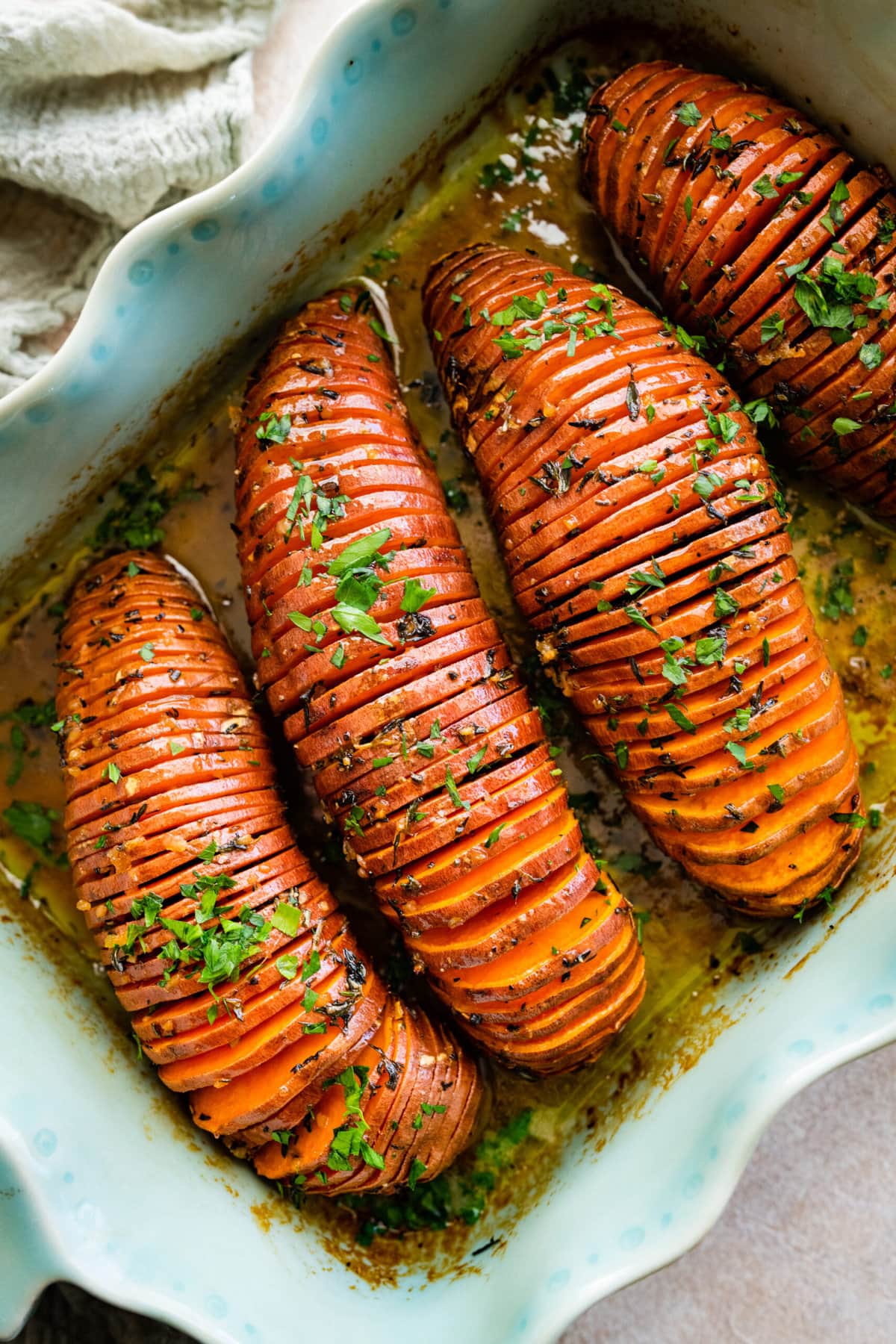 How to make Hasselback Sweet Potatoes with Maple Syrup: potatoes after they are done baking in a teal baking dish. Add fresh parsley for garnish.