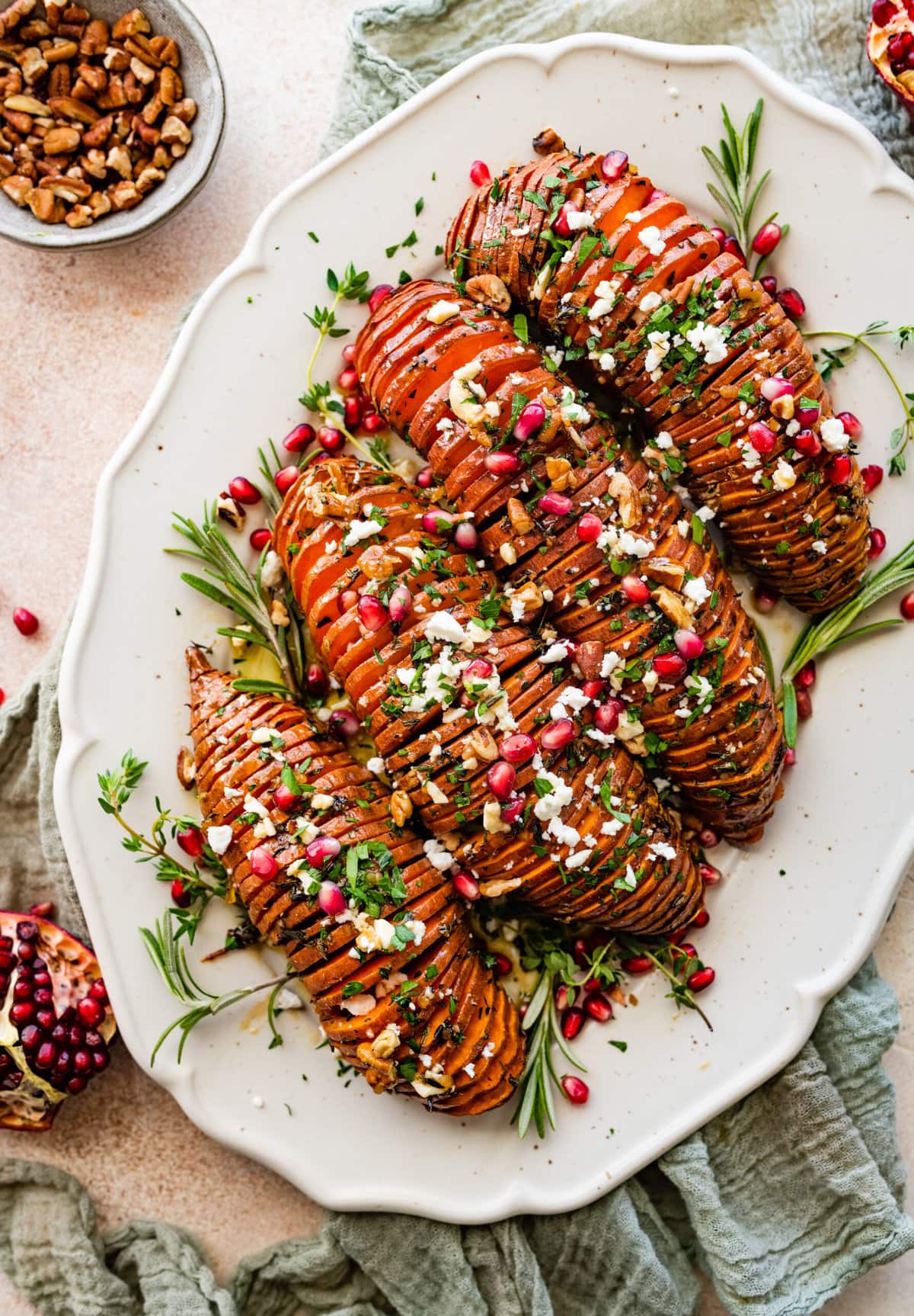 hassleback sweet potatoes on a beautiful white serving platter garnished with fresh herbs and pomegranate seeds.  