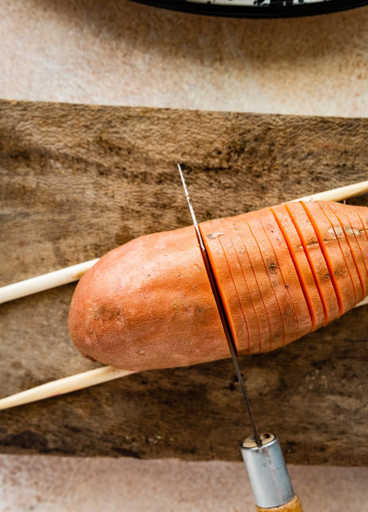 How to make Hasselback Sweet Potatoes with Maple Syrup: cut the potatoes with two wooden sticks one on each side.