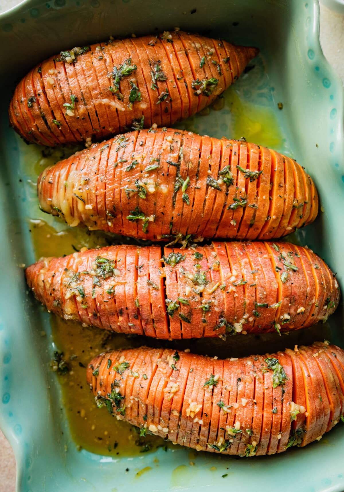 How to make Hasselback Sweet Potatoes with Maple Syrup: seasoned potatoes ready to bake in a teal baking dish.