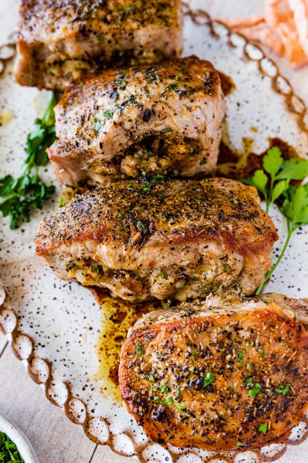 oven baked stuffed pork chops on a large serving platter with herbs as garnish.