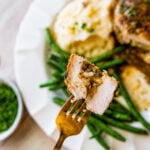 stuffed pork chop cut open to see filling with green beans and mashed potatoes. Bite taken out with a fork.