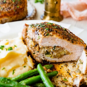 Baked stuffed pork chop on a plate with mashed potatoes and green beans.
