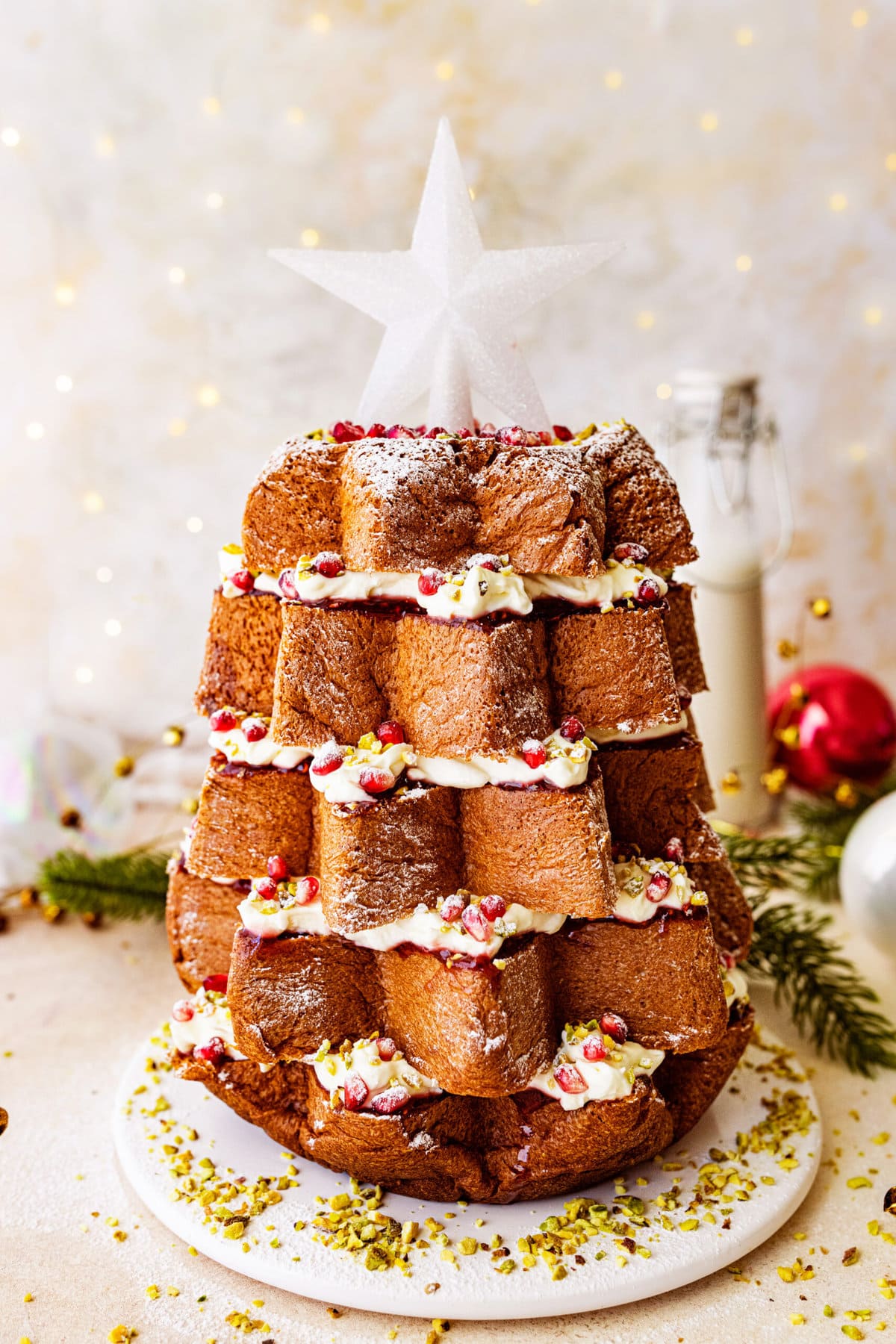 Pandoro Christmas Tree Cake (Italian Christmas Cake)- finished cake decorated with pomegranate seeds and a beautiful white star on top. Christmas. White snowkflake decorations in background.  