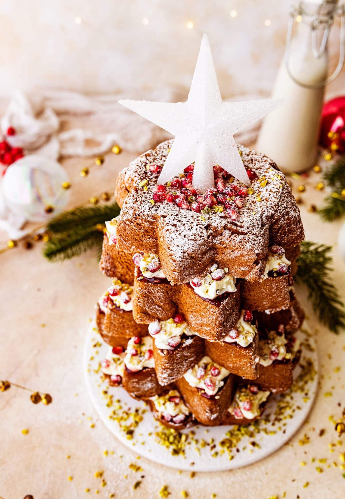 Pandoro Christmas Tree Cake (Italian Christmas Cake)- finished cake decorated with pomegranate seeds and a beautiful white star on top. Christmas. White snowkflake decorations in background.