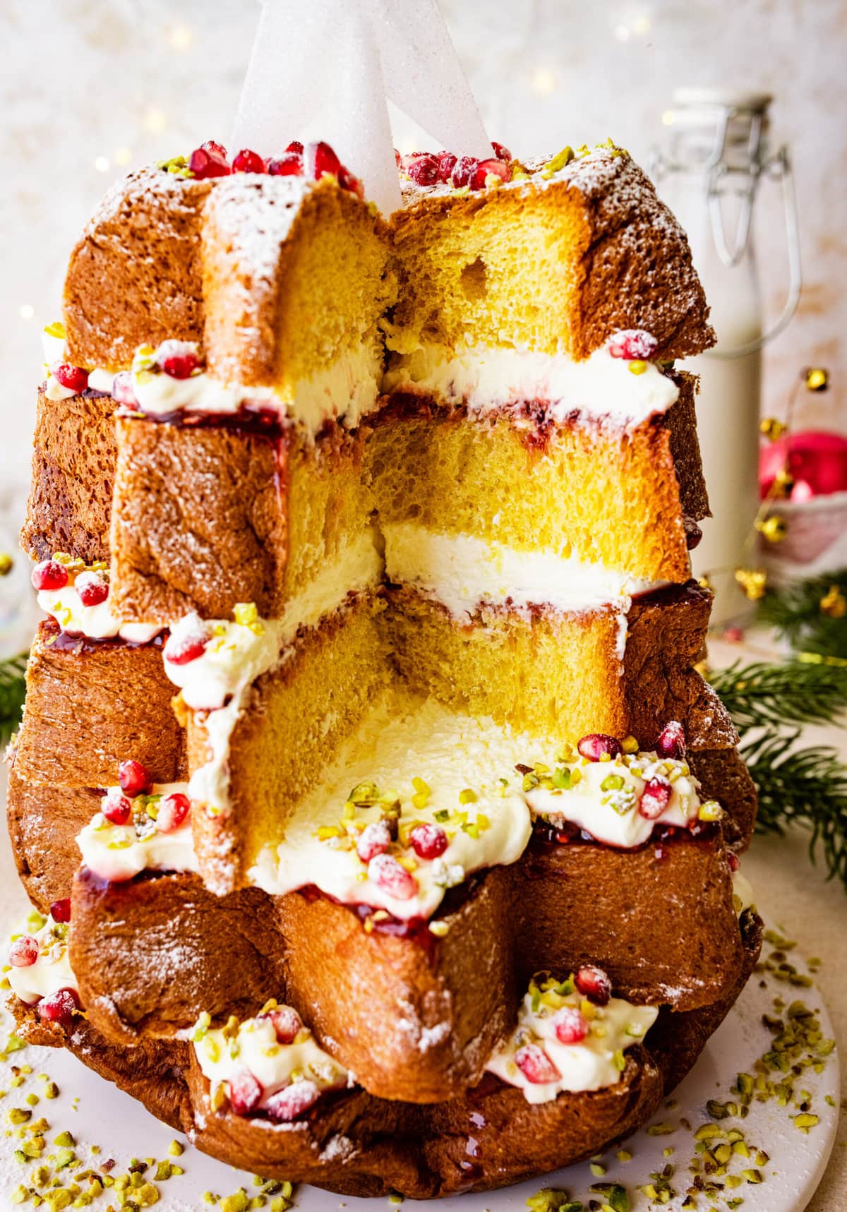 Pandoro Christmas tree cake with star on top and Christmas mood all around with lights and tiny gold bells. Cut a slice and see the middle layers of the cake.