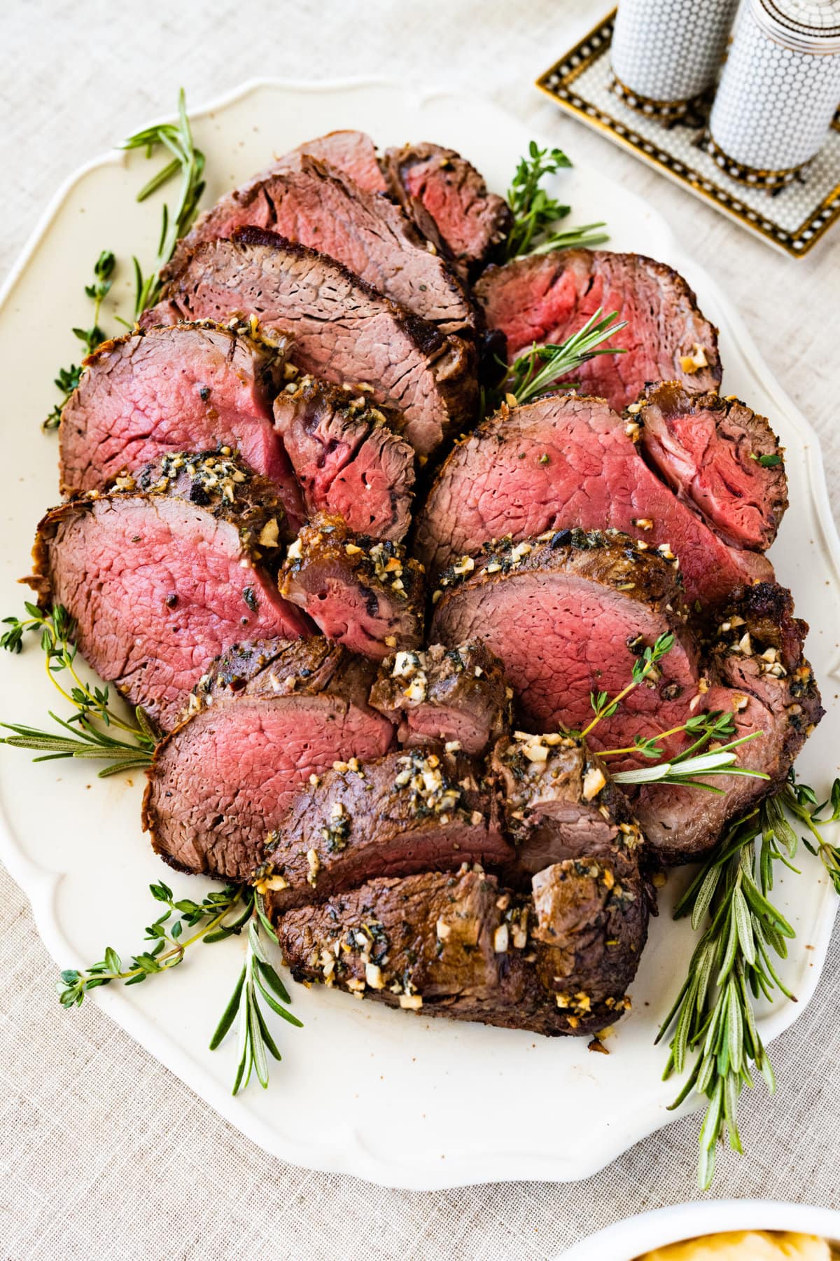 slices of perfect roast beef tenderloin on a pretty white platter with herbs on the side.