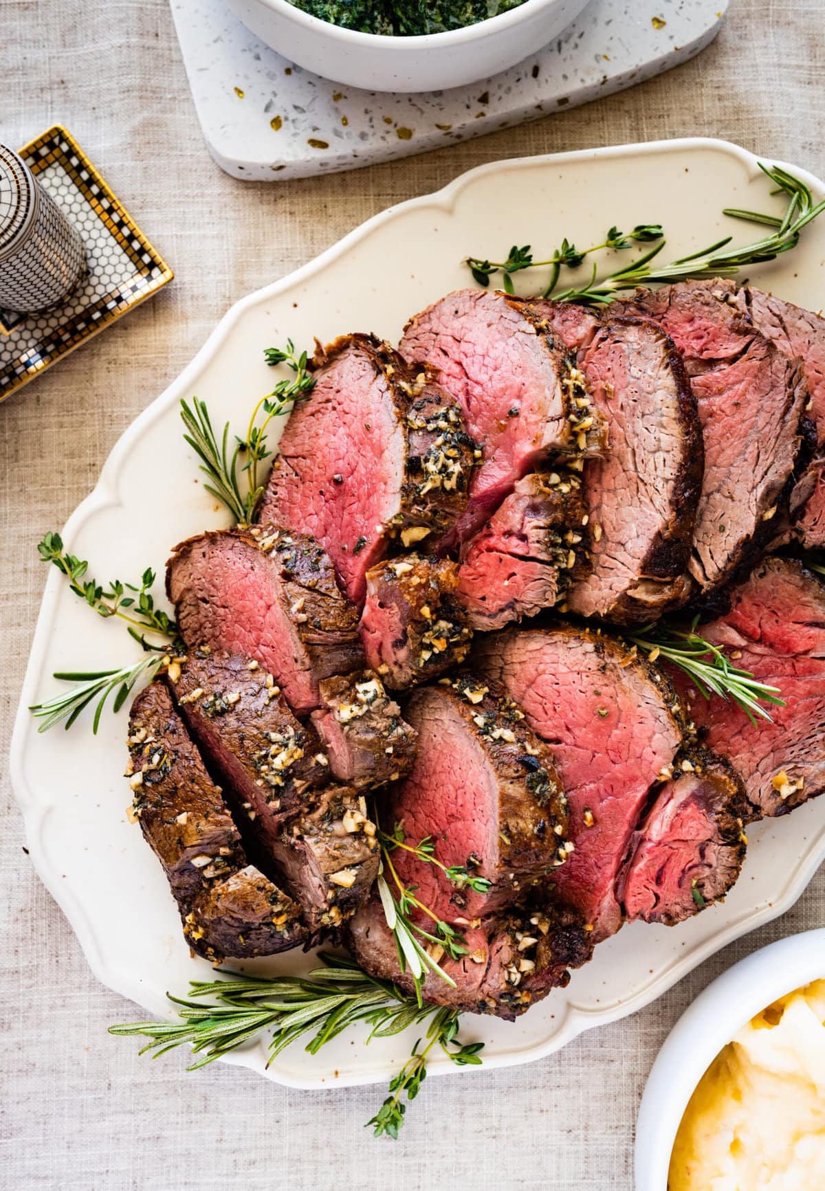 slices of perfect roast beef tenderloin on a pretty white platter with herbs on the side. 