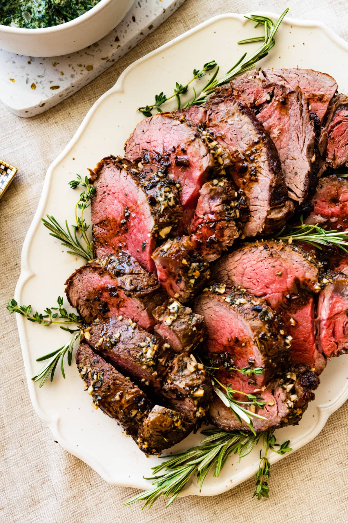perfect roast beef tenderloin on a pretty white platter with herbs on the side.