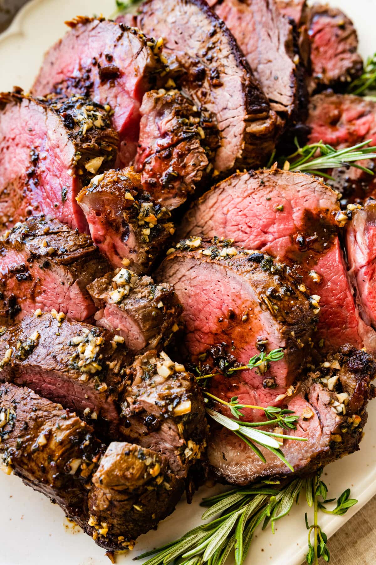 close up of slices of perfect roast beef tenderloin on a pretty white platter with herbs on the side.