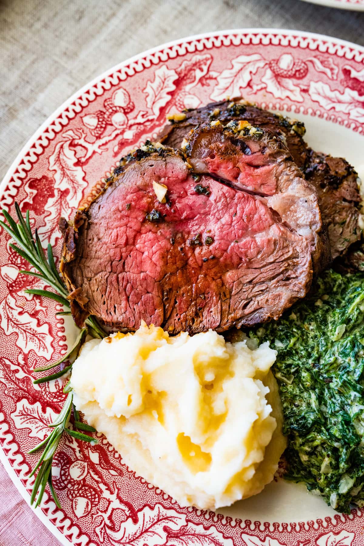 close up of platted roast beef tenderloin with mashed potatoes and creamed spinach. A side of horseradish sauce.