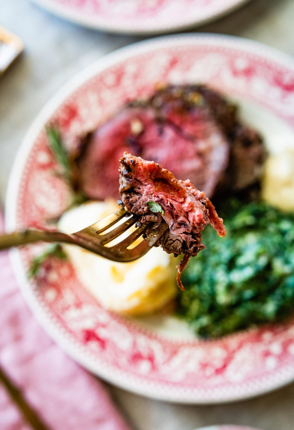 platted roast beef tenderloin with mashed potatoes and creamed spinach. A side of horseradish sauce. Fork holding up a bite of meat.