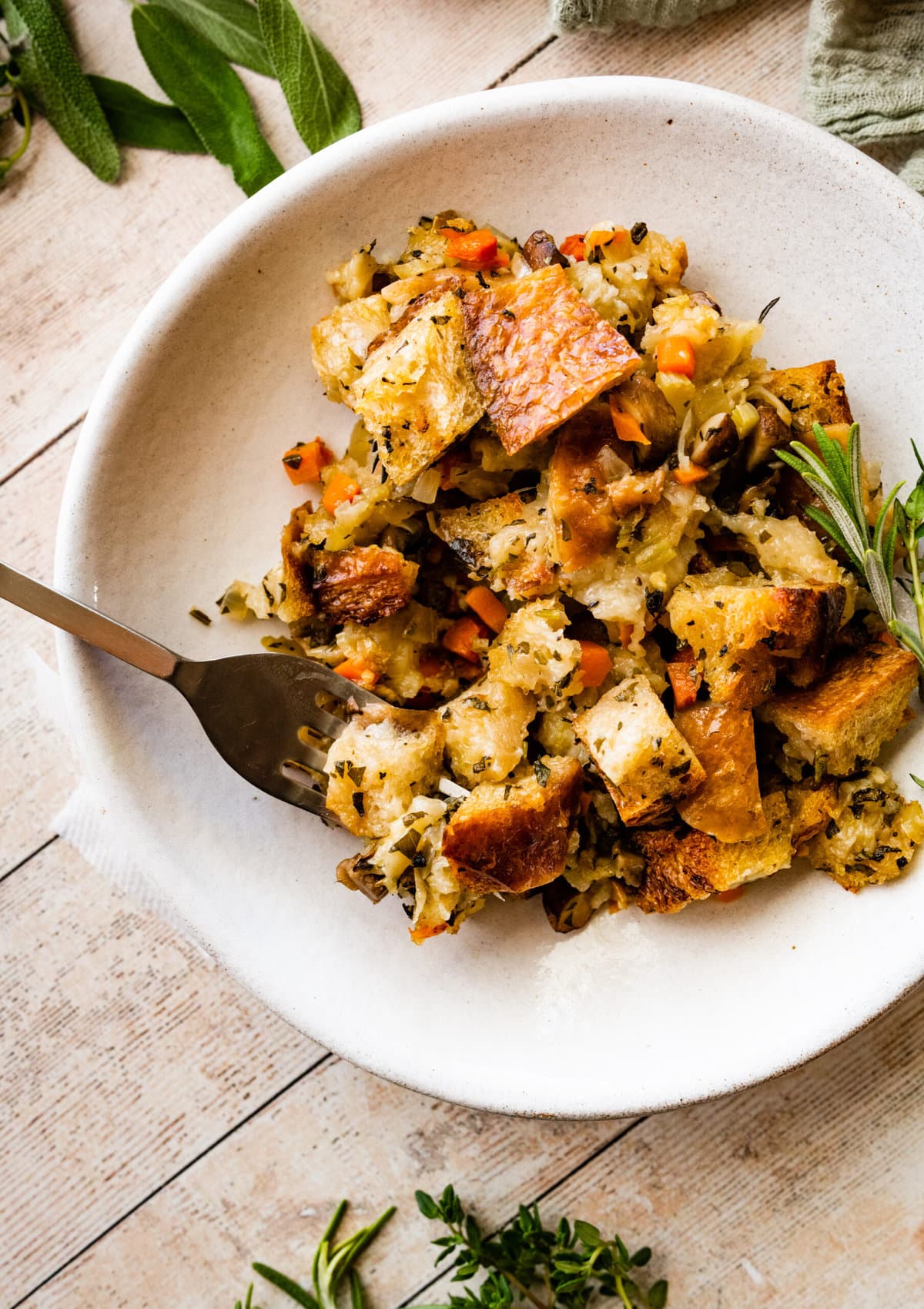 a portion of veg stuffing on a white plate with a fork. Herbs around the plate. Up close of the stuffing.