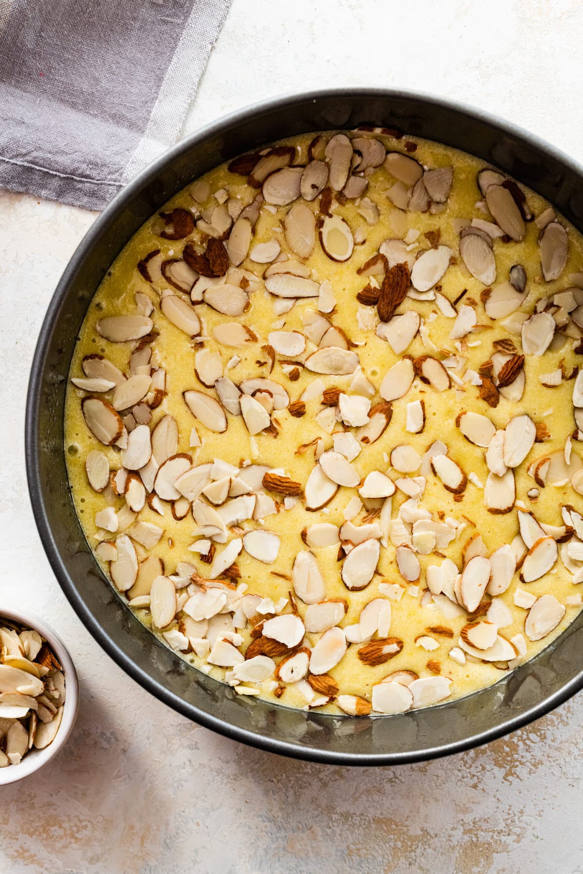 How to make easy almond cake recipe step by step: placing batter in a round metal pan and baking. Sprinkle with sliced almonds.