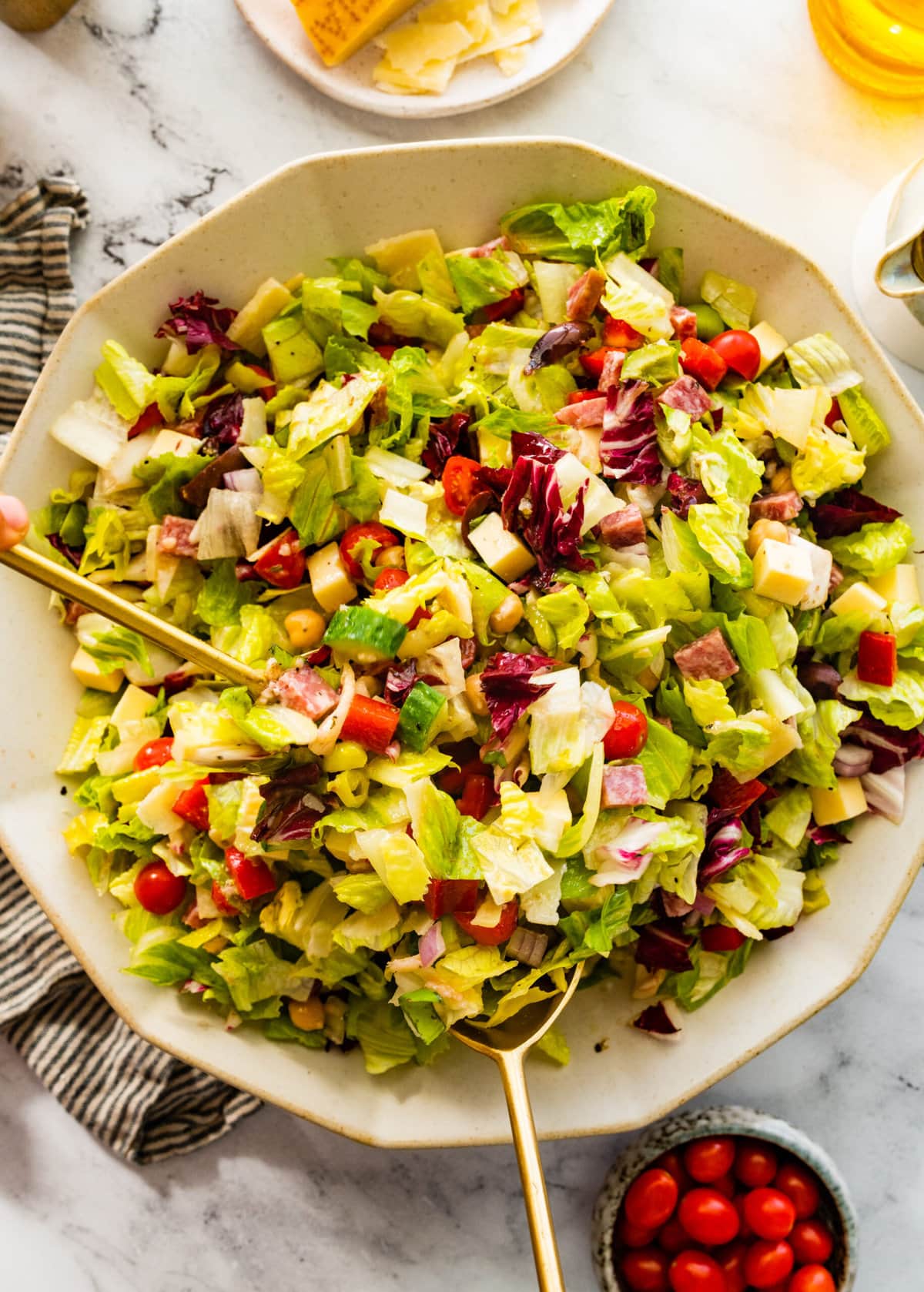 Italian chopped salad tossed with dressing and gold salad servers.