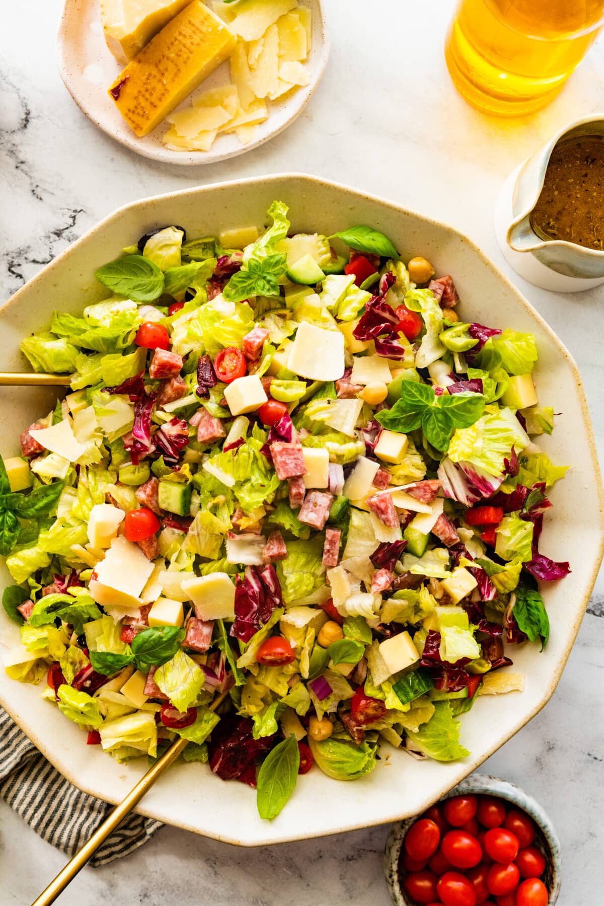 Best Italian Chopped Salad in a white serving bowl with a small jar of tomatoes on the side.