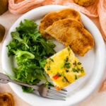 slice of breakfast casserole on a plate with toast and green salad.