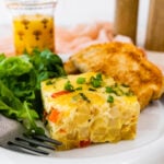 slice of breakfast casserole on a plate with toast and green salad. Side view of slice on the plate.