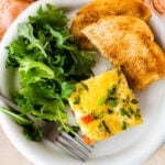 slice of breakfast casserole on a plate with toast and green salad.