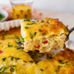 Spoon scooping a piece of breakfast casserole with potato and egg.
