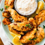pan-fried chicken tenders on a plate with dipping sauce and lemon wedges.