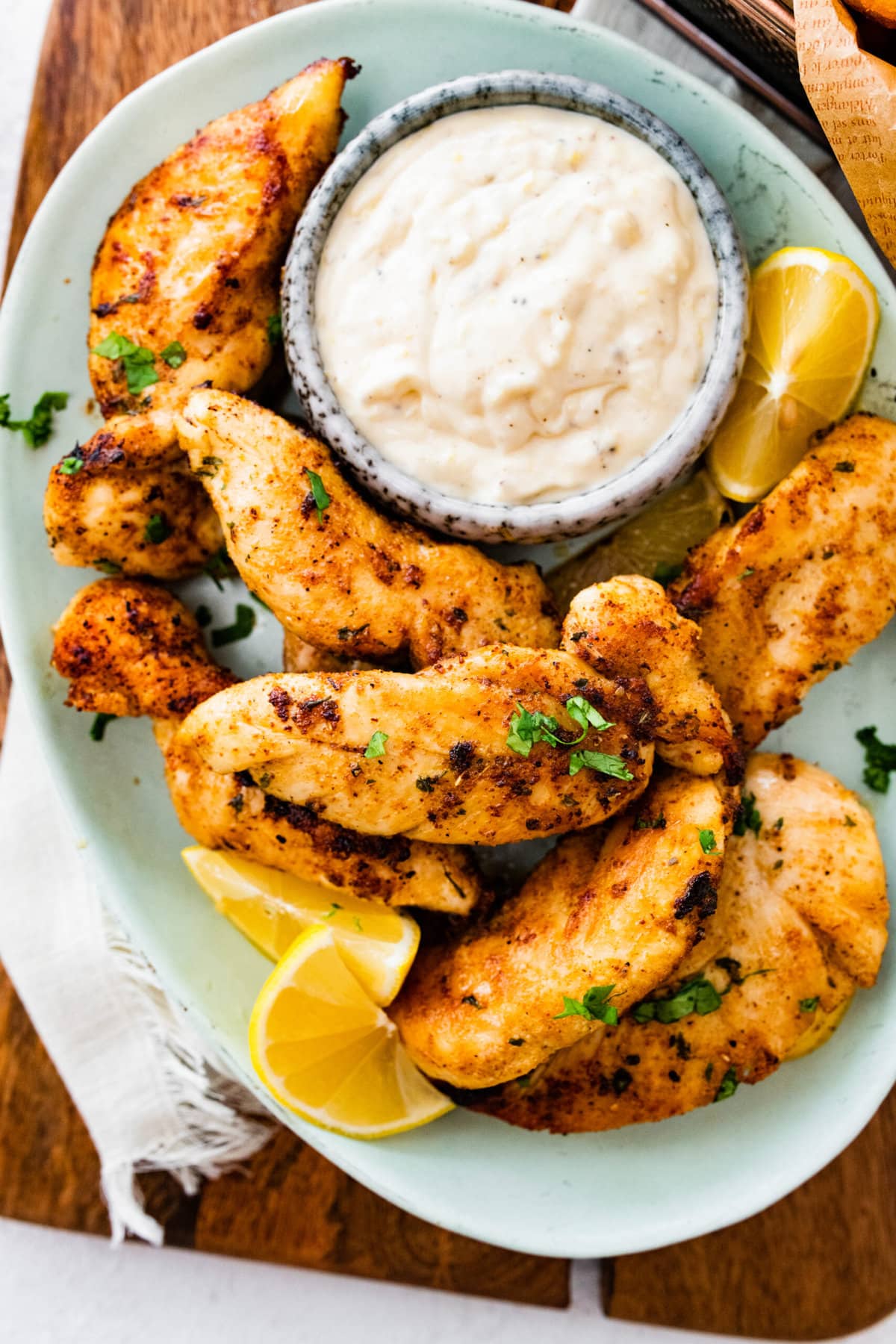 pan-fried chicken tenders on a plate with dipping sauce and lemon wedges.