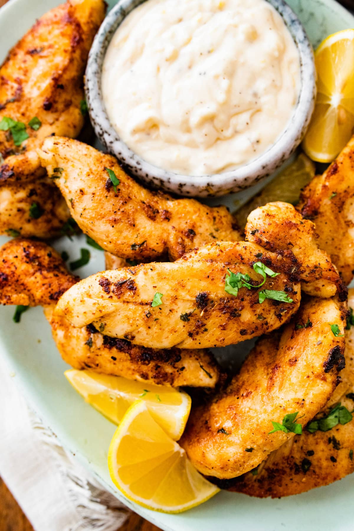 pan-fried chicken tenders on a plate with dipping sauce and lemon wedges.