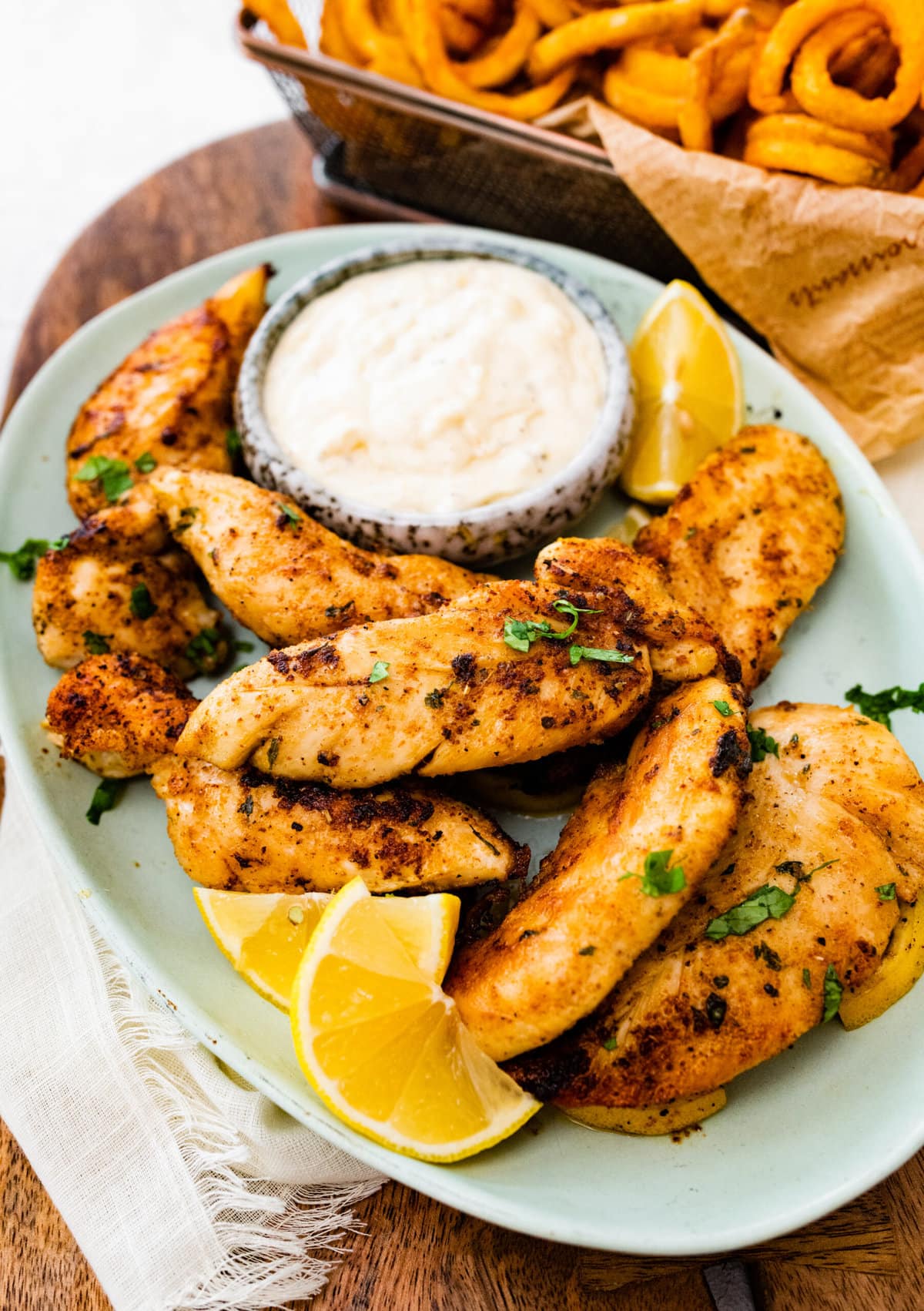 pan-fried chicken tenders on a plate with dipping sauce and lemon wedges.