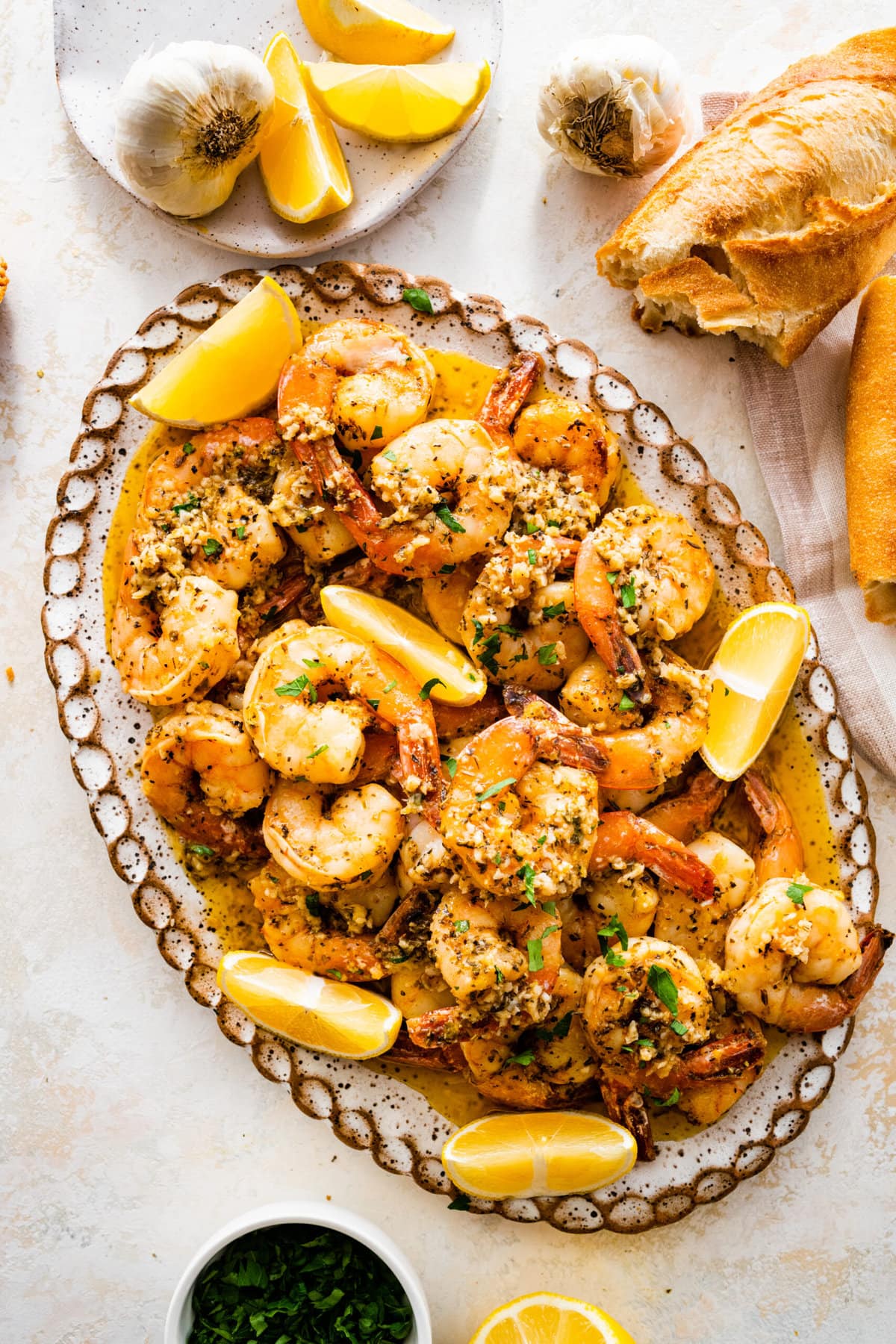 seared shrimp on a serving platter with lemon wedges around it and crusty Italian bread for serving.