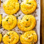 duchess potatoes finished cooking on baking tray. sprinkled with herbs on the top.