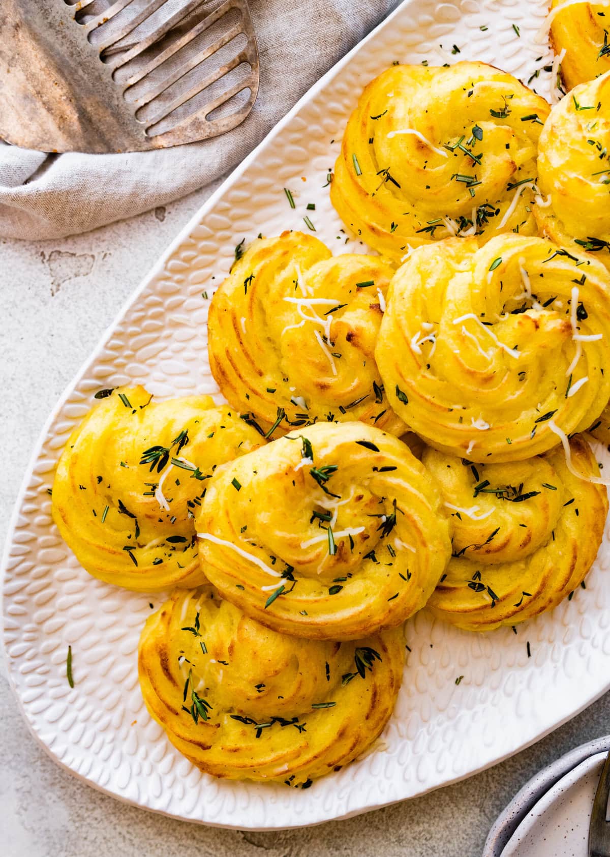 duchess potatoes on a white serving platter. sprinkled with herbs and extra cheese on top.