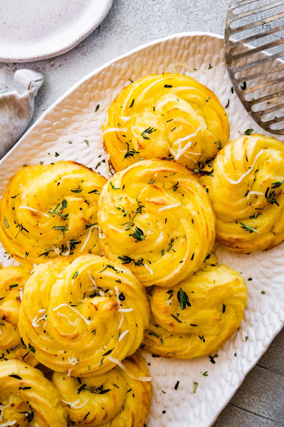 close up of duchess potatoes on a white serving platter. sprinkled with herbs and extra cheese on top. 