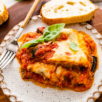 slice of eggplant parmigiano on a plate with a slice of bread on the side.