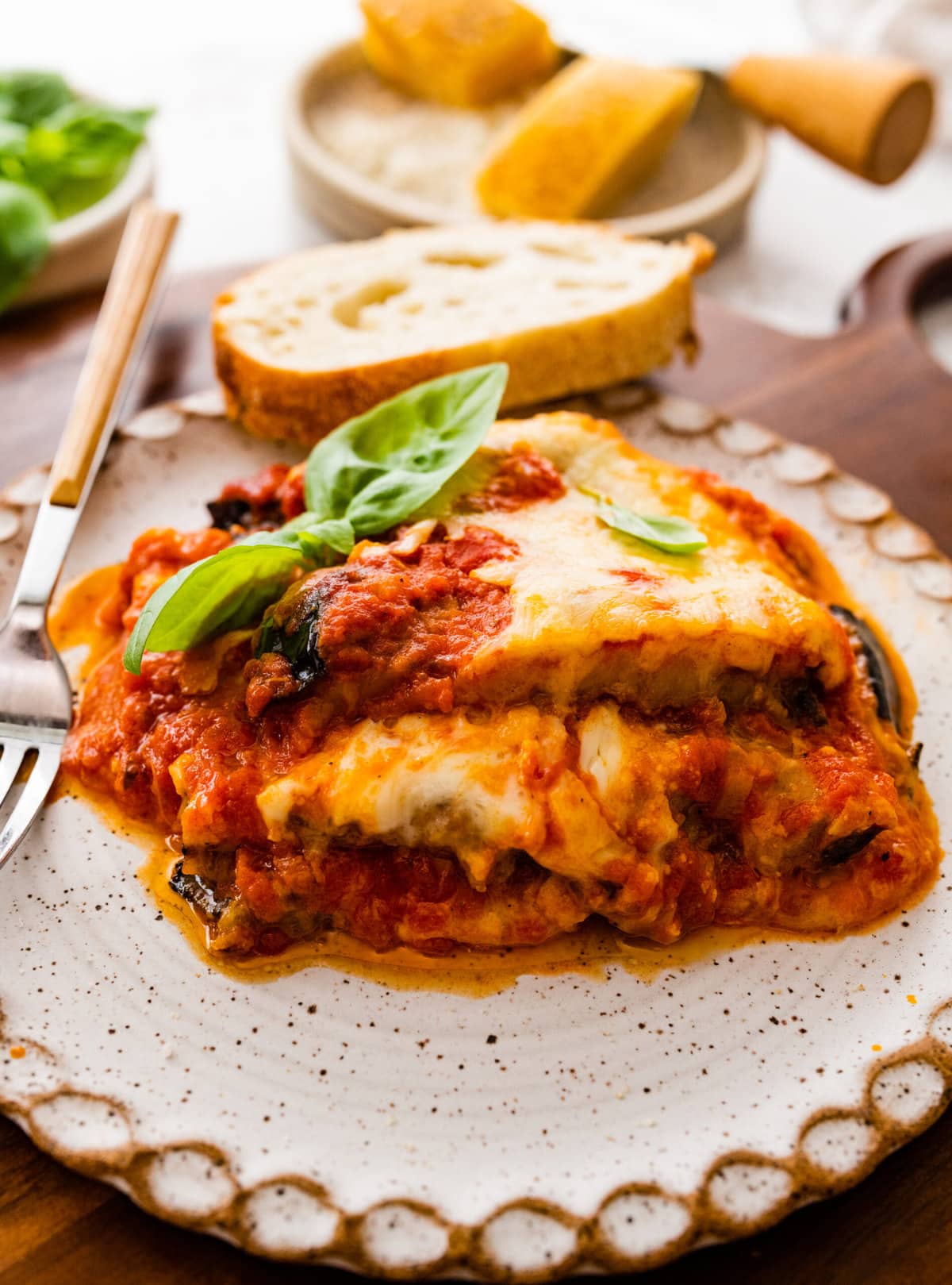 Slice of eggplant parmigiana on a plate with bread and a fork.