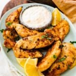 pan-fried chicken tenders on a plate with dipping sauce and lemon wedges.