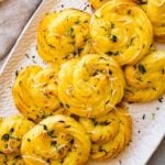 close up of duchess potatoes on a white serving platter. sprinkled with herbs and extra cheese on top.