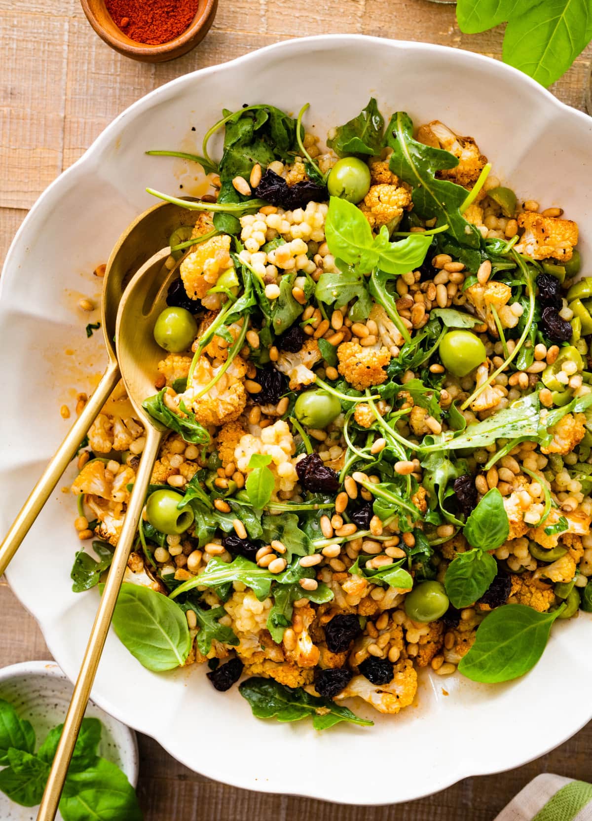 warm fregola salad in a white serving bowl with gold salad servers in the salad ready to serve. 