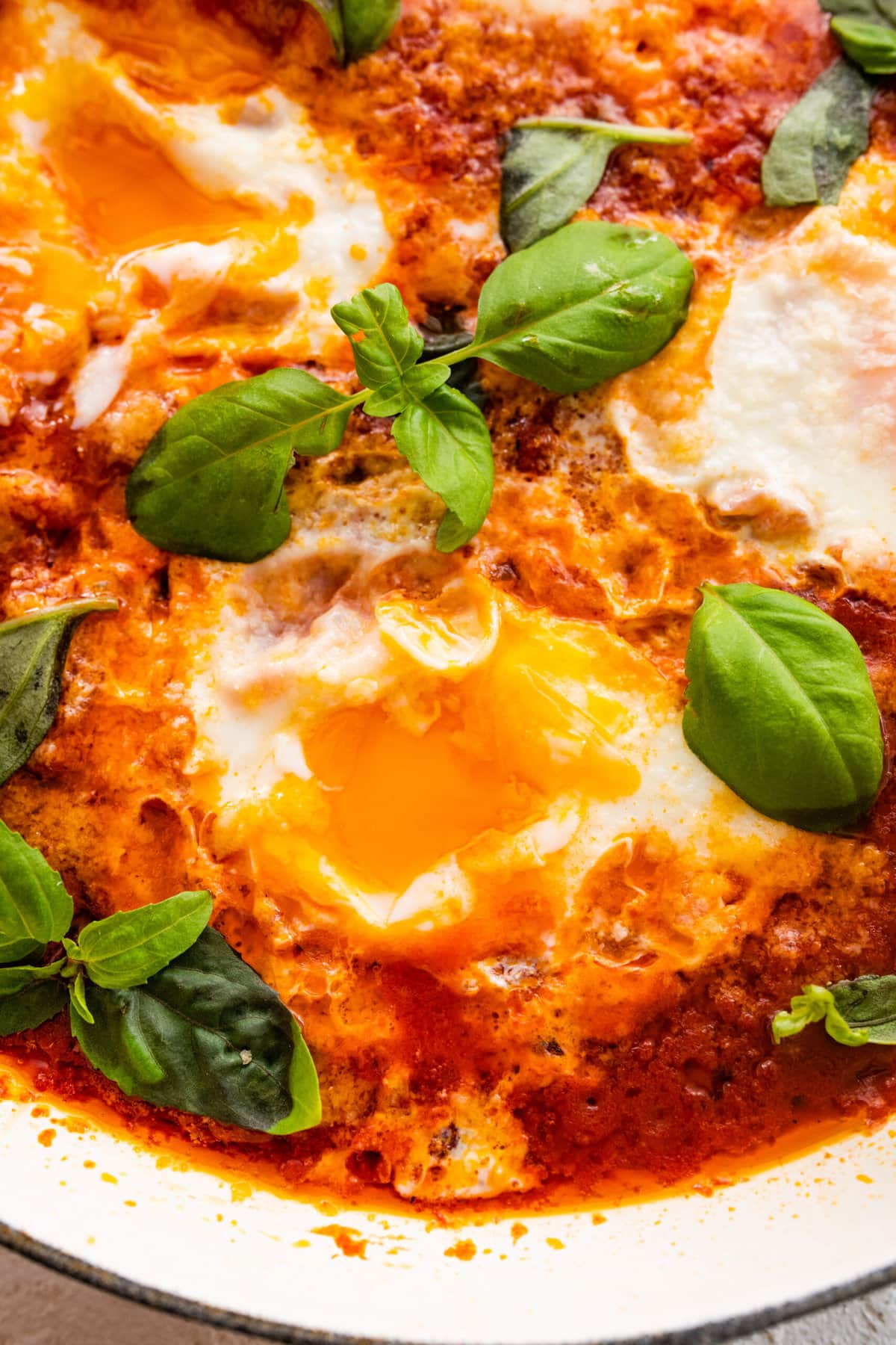 finished eggs in purgatory dish with extra basil as a garnish. Bread on the side for serving and dipping. Egg yolks visible with and dipping bread.