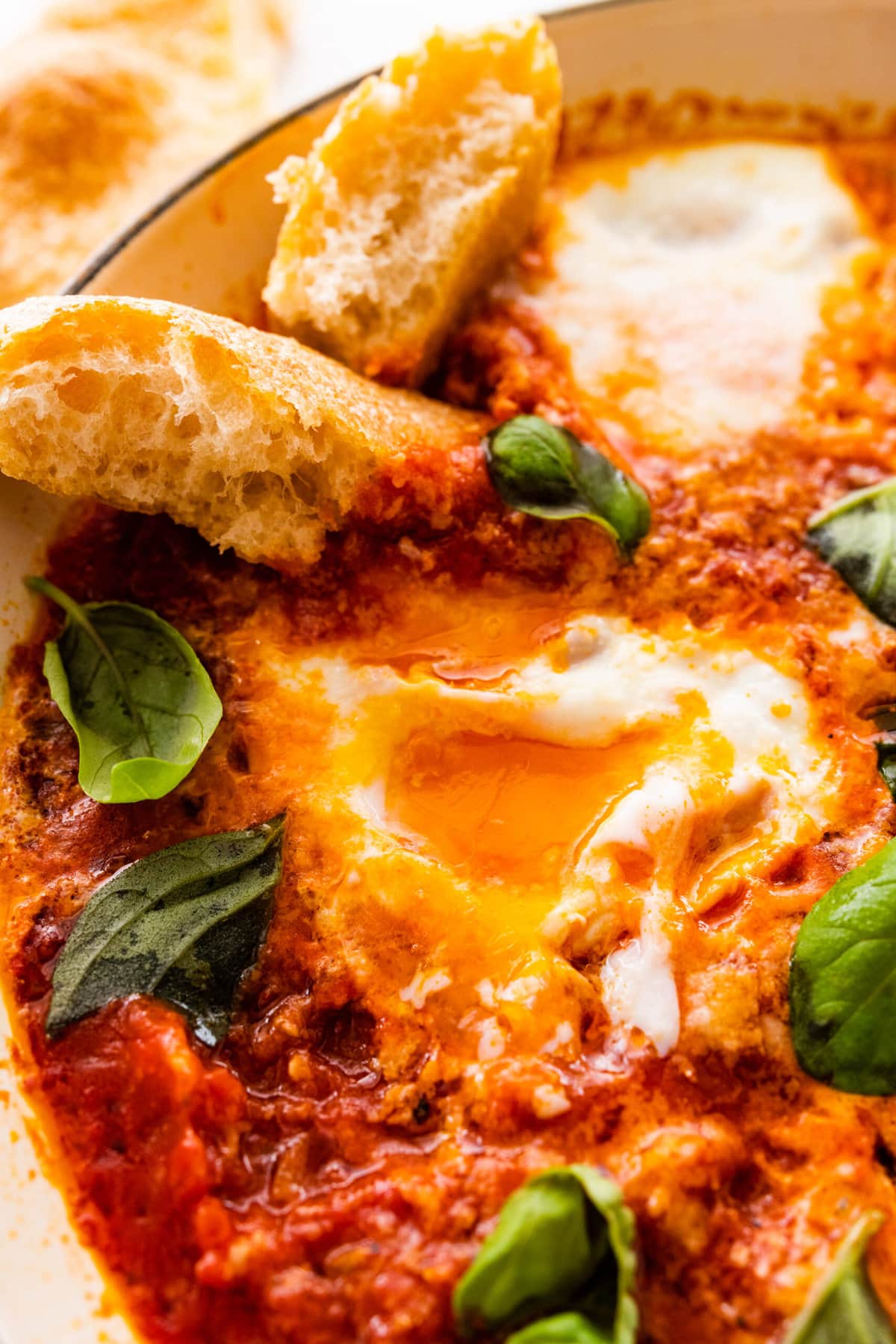 finished eggs in purgatory dish with extra basil as a garnish. Bread on the side for serving and dipping. Egg yolks visible with and dipping bread.