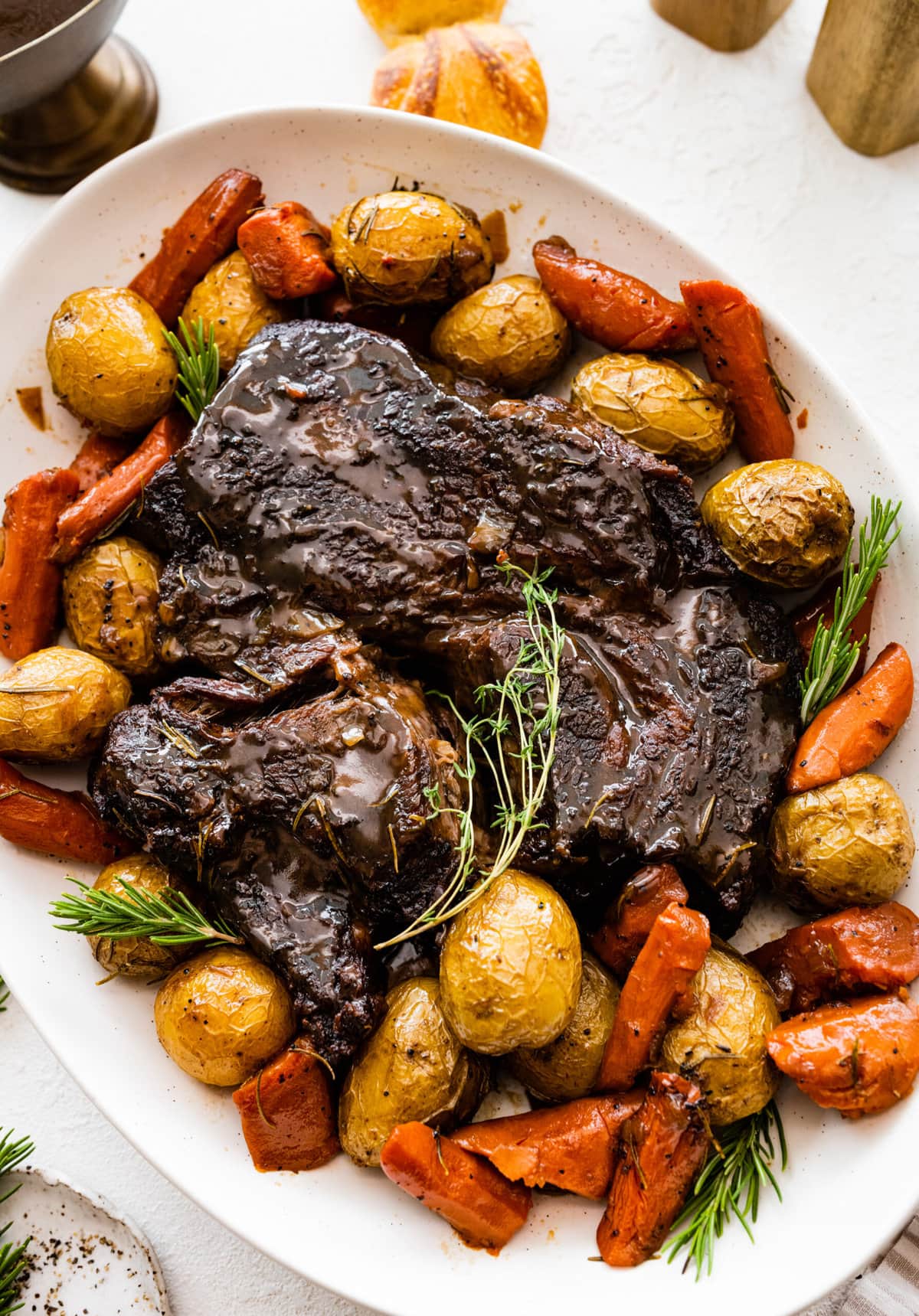 Finished pot roast on a serving platter with vegetables around it. A few fresh herbs on top. 