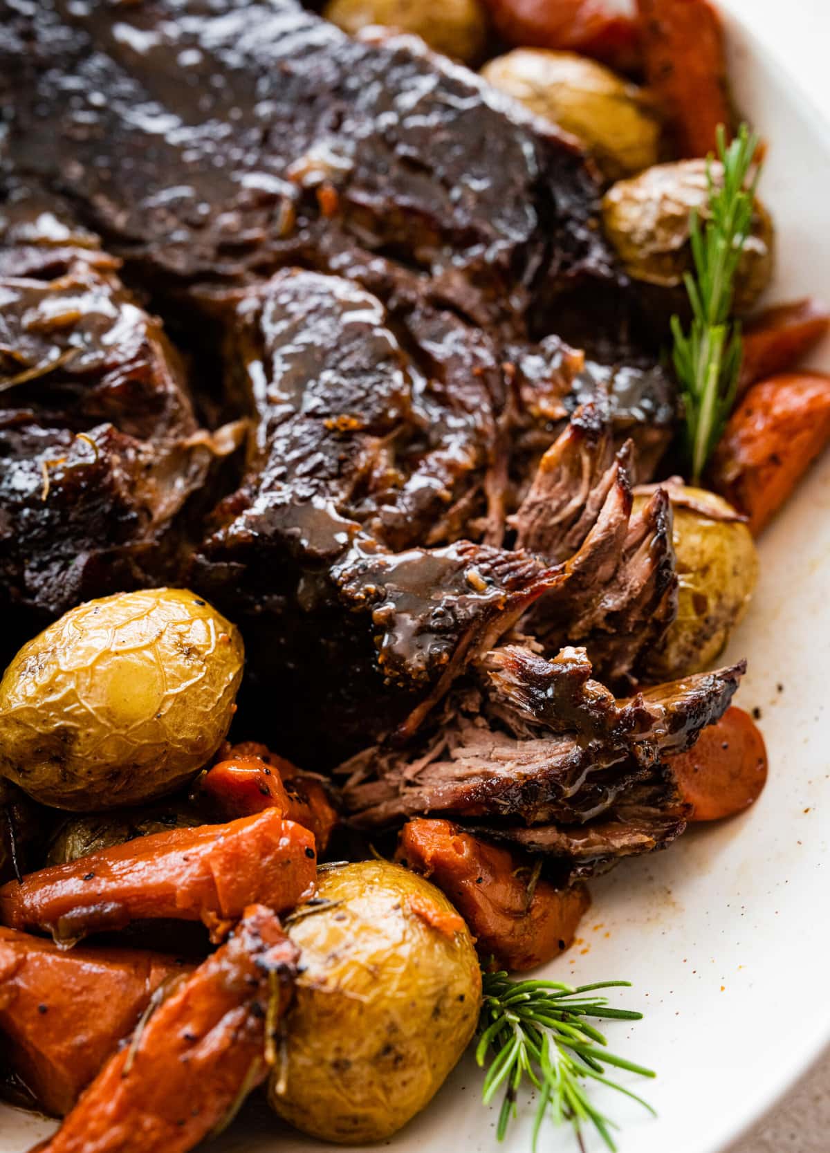 Finished pot roast on a serving platter with vegetables around it. Shredding the pot roast with a fork.